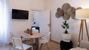Une pièce moderne comprenant une table à manger, des chaises blanches, un téléviseur fixé au mur, des œuvres d’art décoratives et une lampe.