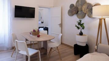 A modern room with a dining table, white chairs, a TV mounted on the wall, decorative wall art, and a lamp.