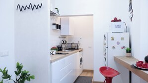 Une cuisine de taille réduite, avec des meubles blancs, un lave-linge, un évier et un réfrigérateur.