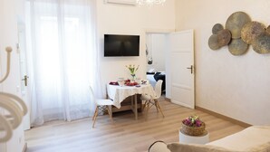 Un salon lumineux comprenant un coin repas, un lustre, un téléviseur à écran plat et un élément décoratif mural.