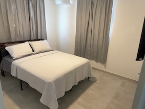A neatly made bed with a white quilt, a wooden headboard, and a wall-mounted air conditioning unit. - Casa Marty. Spacious 4-bedroom house in pleasant Aguadilla with cool AC breeze. (Aguadilla)