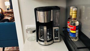 A kitchen with a coffee maker, a glass, and a bottle of Carani on the counter. - Fabulous 3-bedroom MidMod Cottage in charming downtown Cary. (Cary)