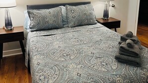 A neatly made bed with patterned bedding, two bedside tables with lamps, and abstract wall art. - Fabulous 3-bedroom MidMod Cottage in charming downtown Cary. (Cary)