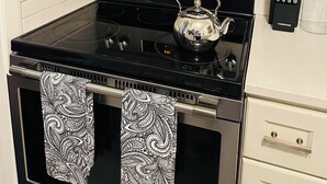 A kitchen with a stainless steel microwave, an oven with a digital clock, and a kettle on the stove. - Fabulous 3-bedroom MidMod Cottage in charming downtown Cary. (Cary)