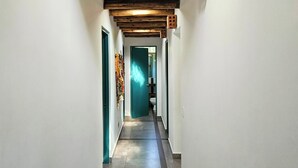 Un couloir étroit aux murs blancs, avec un plafond en bois et une porte verte au fond.