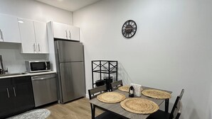 A modern kitchen with white cabinets, a stainless steel refrigerator, and a microwave. There is a dining table with black chairs and woven placemats. - Modern Basement Suite in trendy location in South Winnipeg, near UManitoba (Winnipeg)