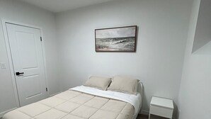 A bedroom with a bed, a nightstand, a painting, and a door. - Modern Basement Suite in trendy location in South Winnipeg, near UManitoba (Winnipeg)