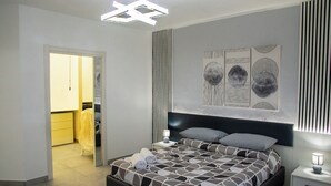 Moderni makuuhuone, jossa on suuri sänky, yöpöytä, seinälle ripustettu taideteos ja kattovalaisin.