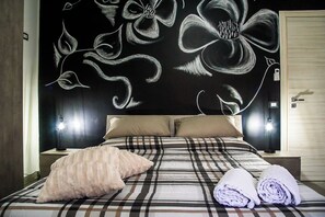 A bedroom with a large bed, two pillows, a blanket, and two rolled towels. - Vacation home just a few meters from the historic center of Agrigento. (Agrigento)
