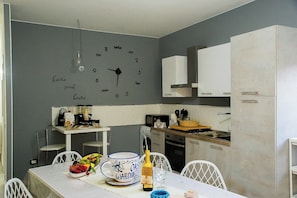 A modern kitchen with a clock on the wall, white cabinets, and a dining area with a table set for two. - Vacation home just a few meters from the historic center of Agrigento. (Agrigento)