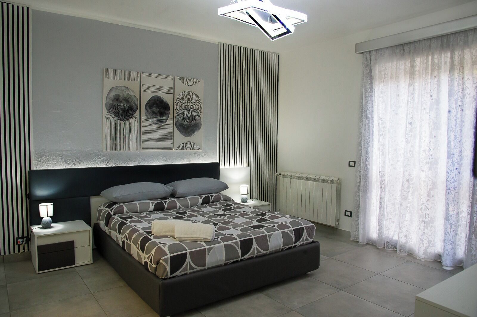 A modern bedroom with a large bed, a bedside table with a lamp, and a wall-mounted artwork.