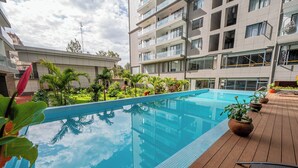 Een modern hotel met een dakzwembad zonder rand, omgeven door weelderige begroeiing en potplanten.