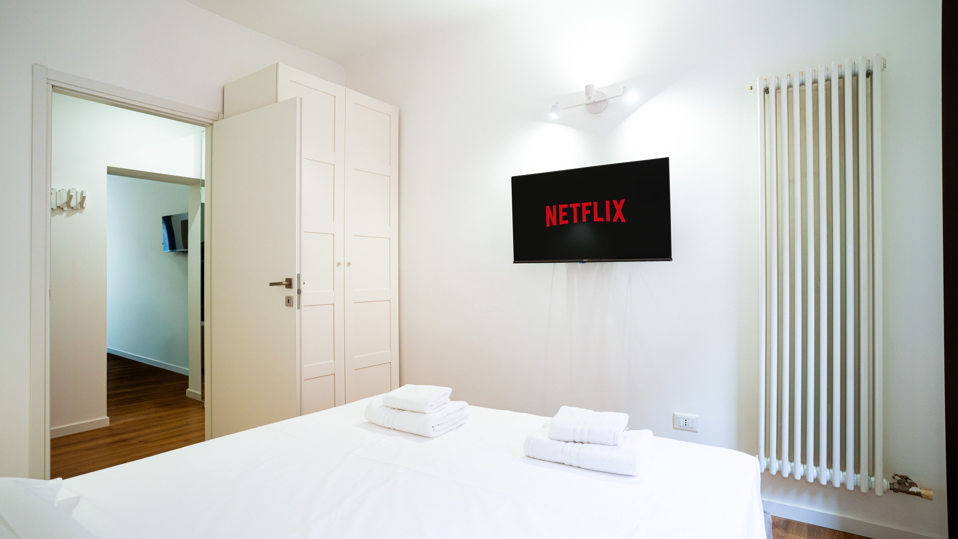 A hotel room with a bed, a TV mounted on the wall, and a closet.