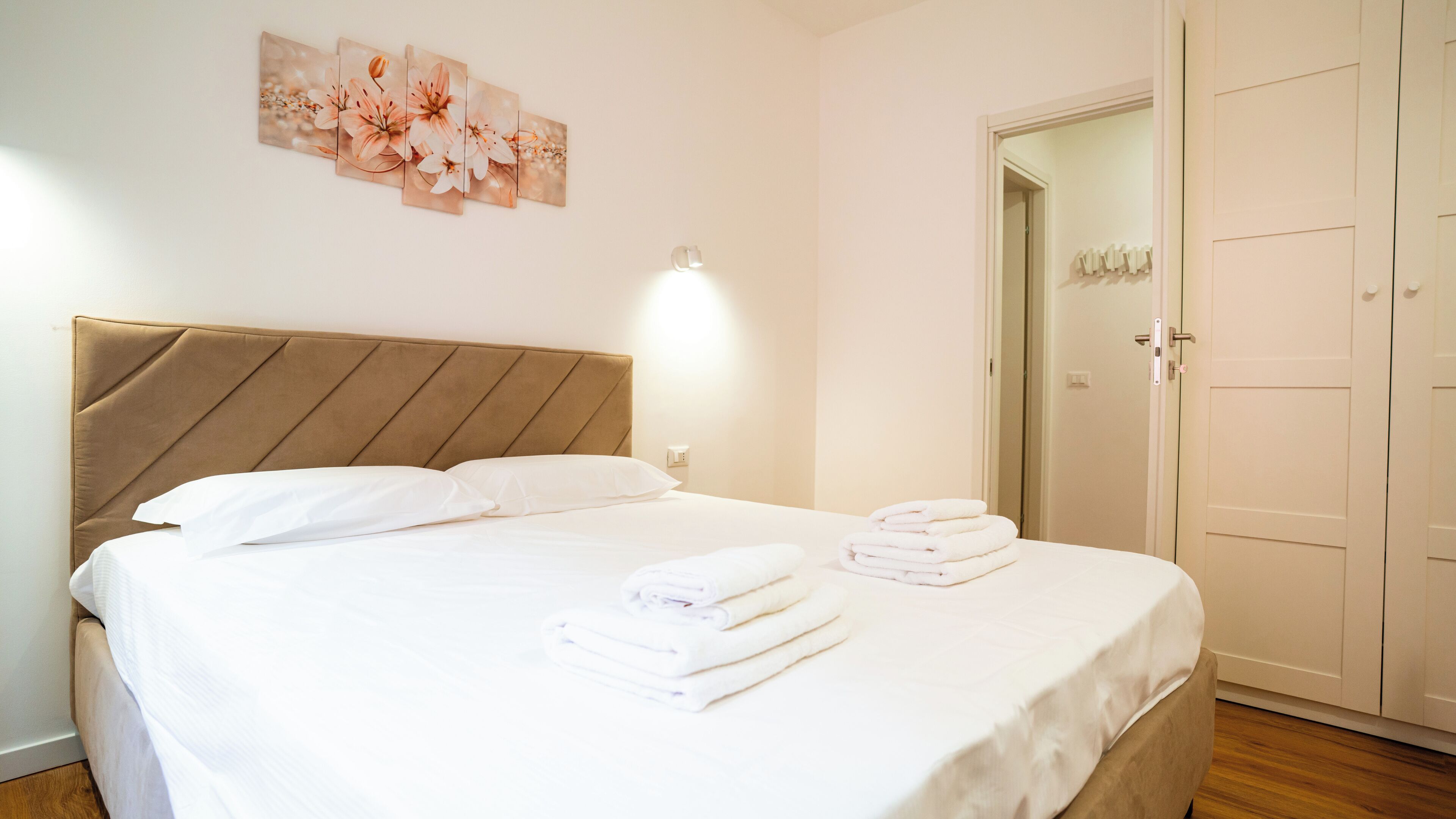 A neatly made bed with white linens and towels, a headboard, and a wall-mounted light fixture.