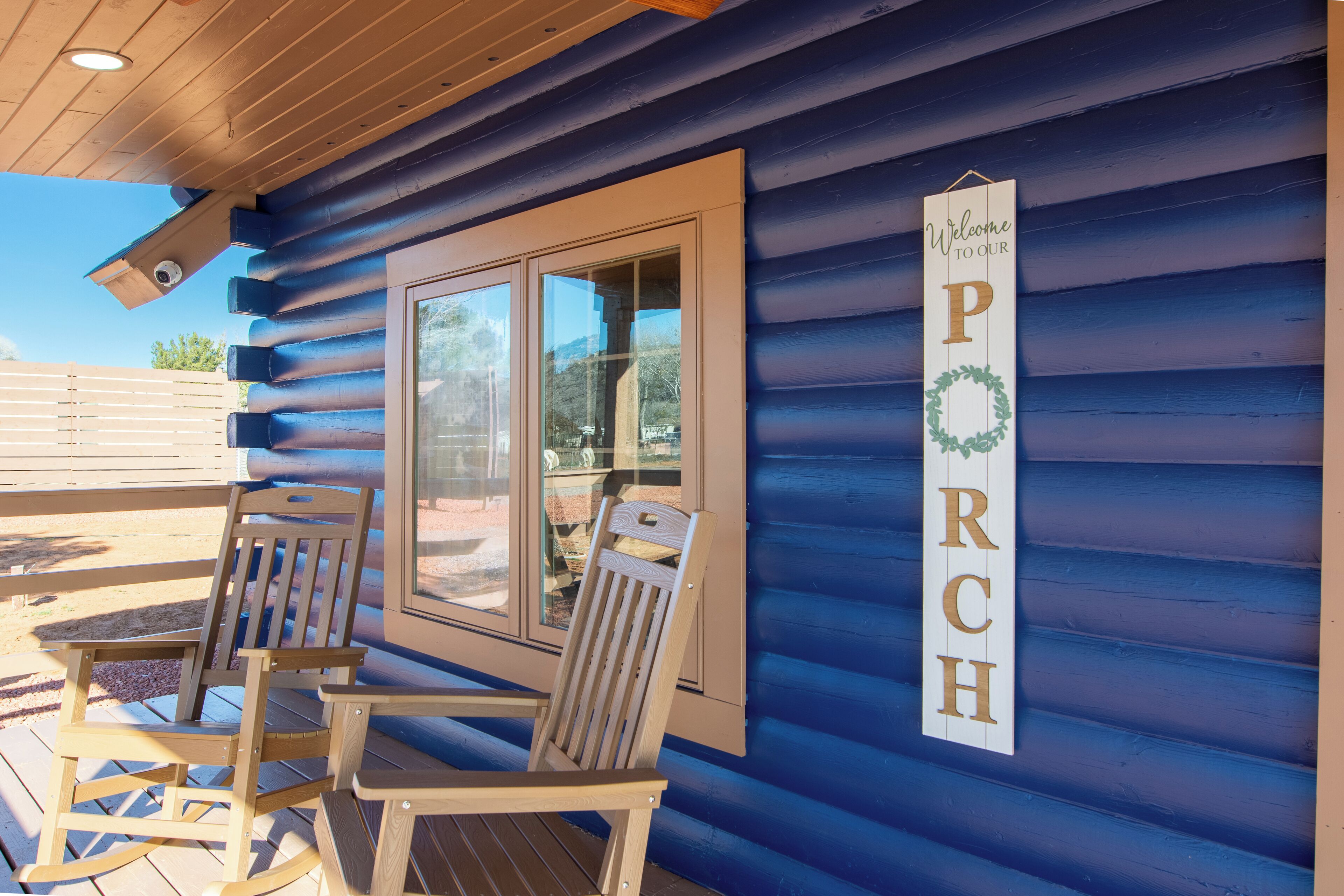 Une cabane en bois dotée d’un porche où se trouvent deux fauteuils à bascule et une pancarte sur laquelle on peut lire : « Bienvenue chez nous ».