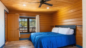 Una camera da letto con soffitto in legno, un letto con biancheria azzurra e una finestra vista alberi.