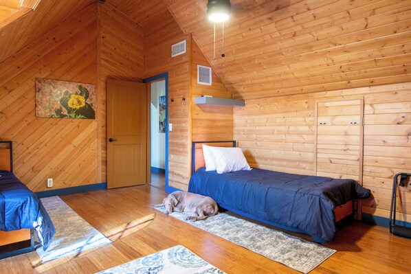 A cozy room with wooden walls, a bed, a dog, and a door leading to another room.
