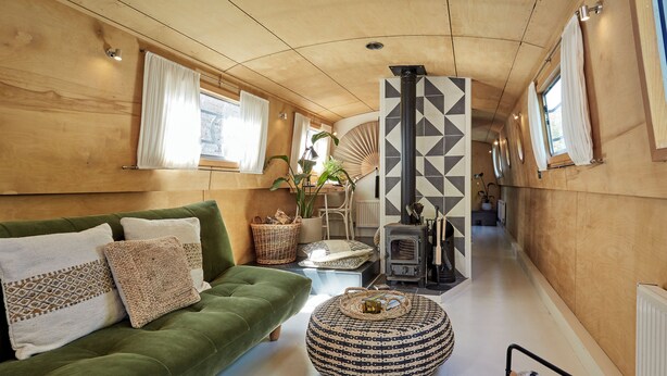 Ein gemütliches Interieur mit einem grünen Sofa, einem gewebten Pouf und einem Holzofen.