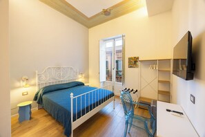 A bedroom with a bed, bedside table, lamp, window, and a TV mounted on the wall. - Rosalia e le altre (Palermo)