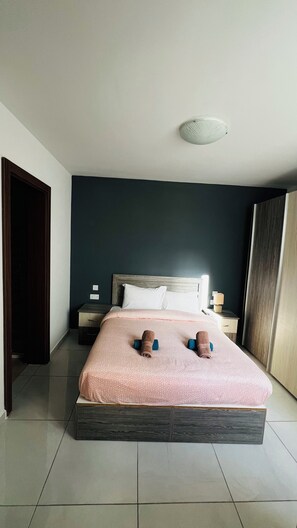 A neatly made bed with a pink patterned bedspread and two rolled towels on blue supports. - Fleur de- Lys (Birkirkara)