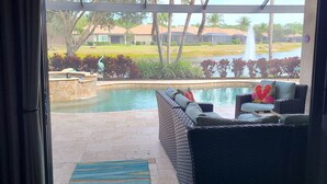 A view from inside a room to a pool area with a ceiling fan, a wicker sofa, and a decorative pillow. - Beautiful 2-bedroom house in a perfect Bonita Springs location (Bonita Springs)