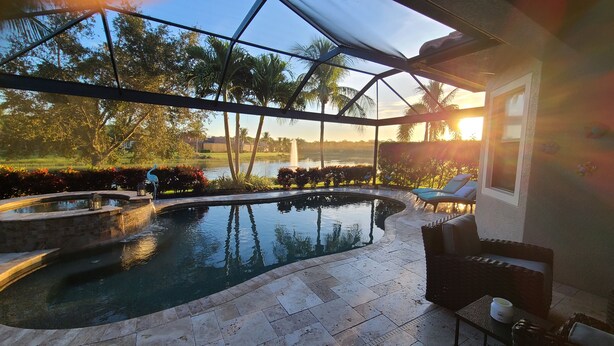 A swimming pool with a glass enclosure, surrounded by a landscaped garden and a view of a body of water. - Beautiful 2-bedroom house in a perfect Bonita Springs location (Bonita Springs)