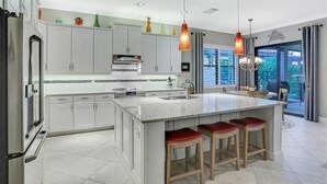 A modern kitchen with white cabinets, a large island with stools, pendant lighting, and a view to the outside. - Beautiful 2-bedroom house in a perfect Bonita Springs location (Bonita Springs)