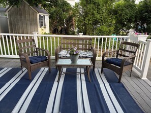 Una terraza con sillas de mimbre y una mesa, rodeada por una barandilla blanca.