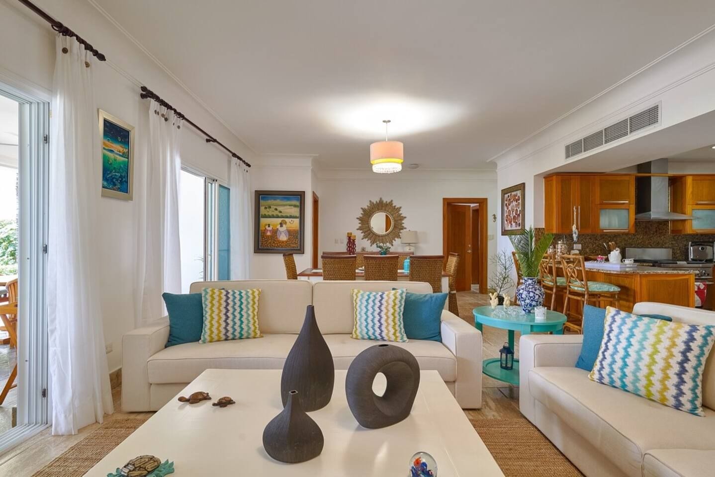 Een woonkamer met een zithoek, een salontafel met decoratieve items, een eethoek met stoelen, en een keuken zichtbaar op de achtergrond.