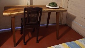 Ett litet rum med ett skrivbord i trä, en stol, en tv som är monterad på väggen och en inramad tavla ovanför skrivbordet.