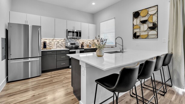 Cozinha moderna com ilha central, eletrodomésticos de aço inoxidável e banquetas pretas.