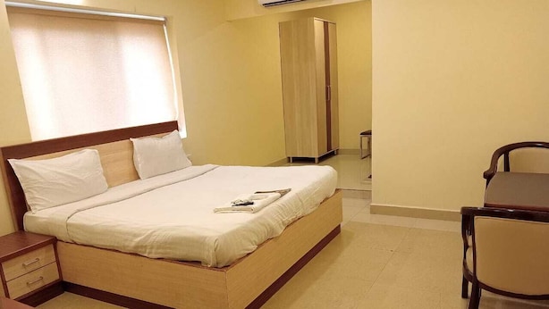 A neatly arranged hotel room with a bed, bedside table, chair, and a wardrobe. - Hotel Sri Sai Regency (Hyderabad)