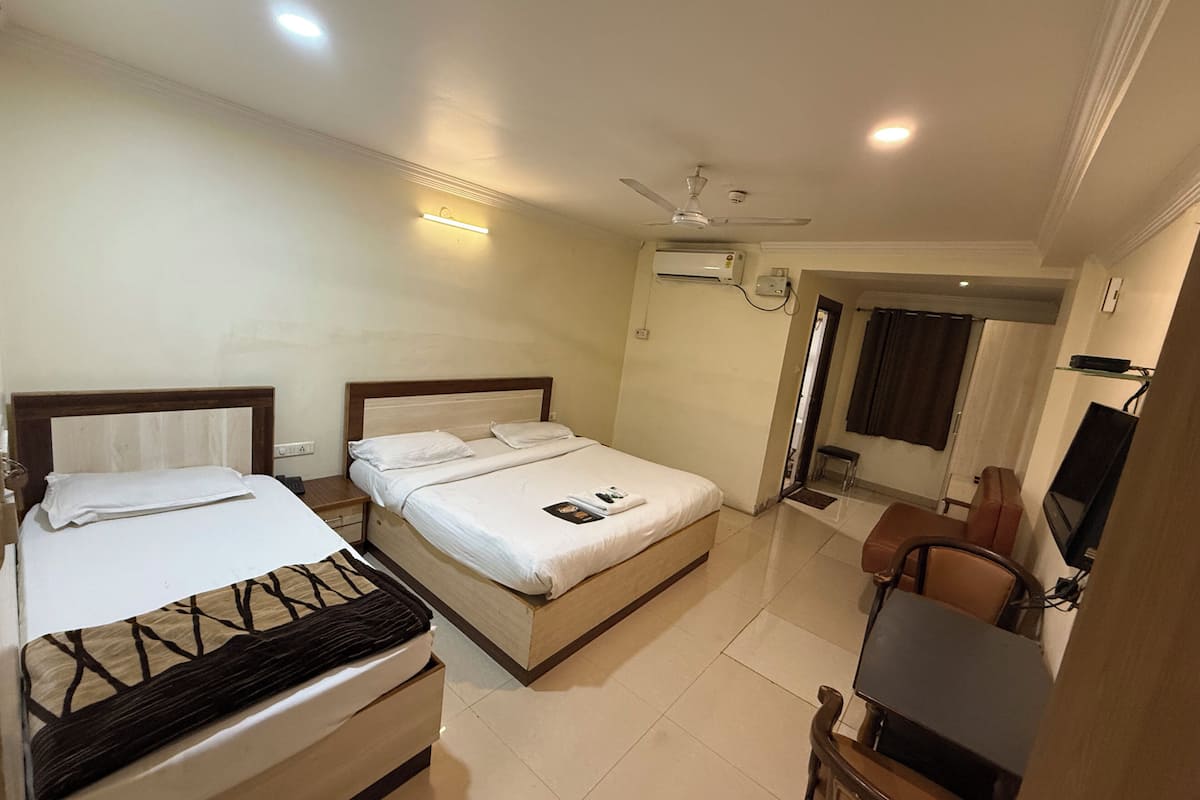 A hotel room with two beds, a desk, a chair, a television, and an air conditioning unit.