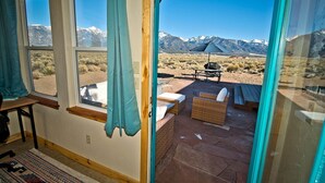 A room with large windows, a view of a desert landscape with mountains, and outdoor furniture. - Bluebird Trail Retreat: Off-Grid & Dark Skies (Saguache County)
