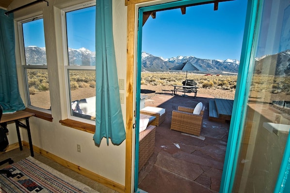 A room with large windows, a view of a desert landscape with mountains, and outdoor furniture.