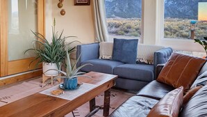 A living room with a wooden coffee table, leather sofa, and a view of mountains through large windows. - Bluebird Trail Retreat: Off-Grid & Dark Skies (Saguache County)