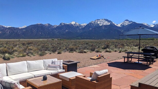 An outdoor patio with wicker furniture, a barbecue grill, and a view of snow-capped mountains. - Bluebird Trail Retreat: Off-Grid & Dark Skies (Saguache County)