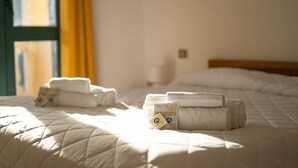 Quarto de hotel com duas camas, cada uma com toalhas dobradas e um pequeno cartão sobre a cama.