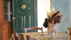 Mesa de jantar com um arranjo floral, uma porta verde ao fundo e cadeiras de madeira.
