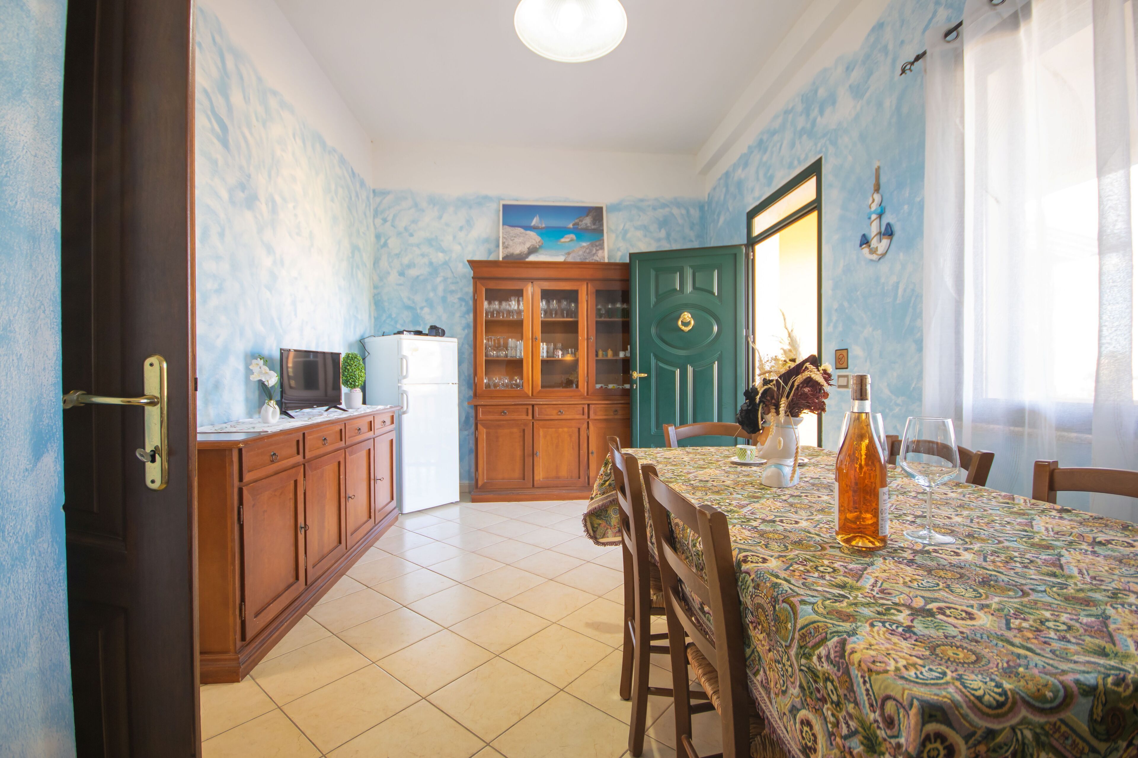 Comedor con mesa lista para dos, aparador con cristalería y puerta con picaporte decorativo.