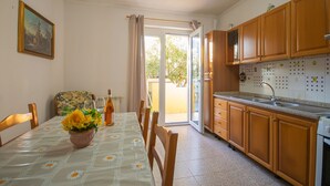 A dining area with a table set for four, a kitchen with wooden cabinets, and a sliding glass door leading to an outdoor area. - Villa Mirto 2 - Two Bedroom Apartment, Sleeps 4 (San Giovanni)