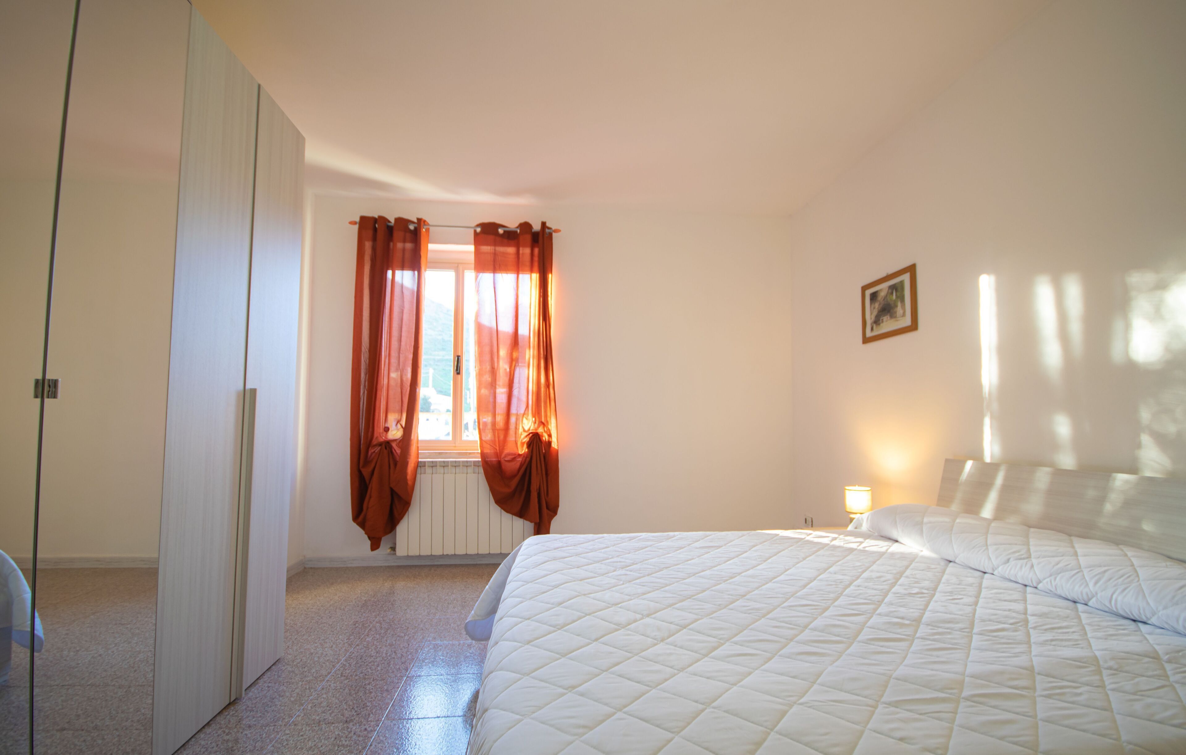 A bedroom with a bed, a nightstand, a lamp, a window with curtains, and a door.