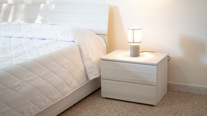 A neatly made bed with a white quilt and a bedside lamp on a wooden nightstand. - Villa Mirto 2 - Two Bedroom Apartment, Sleeps 4 (San Giovanni)
