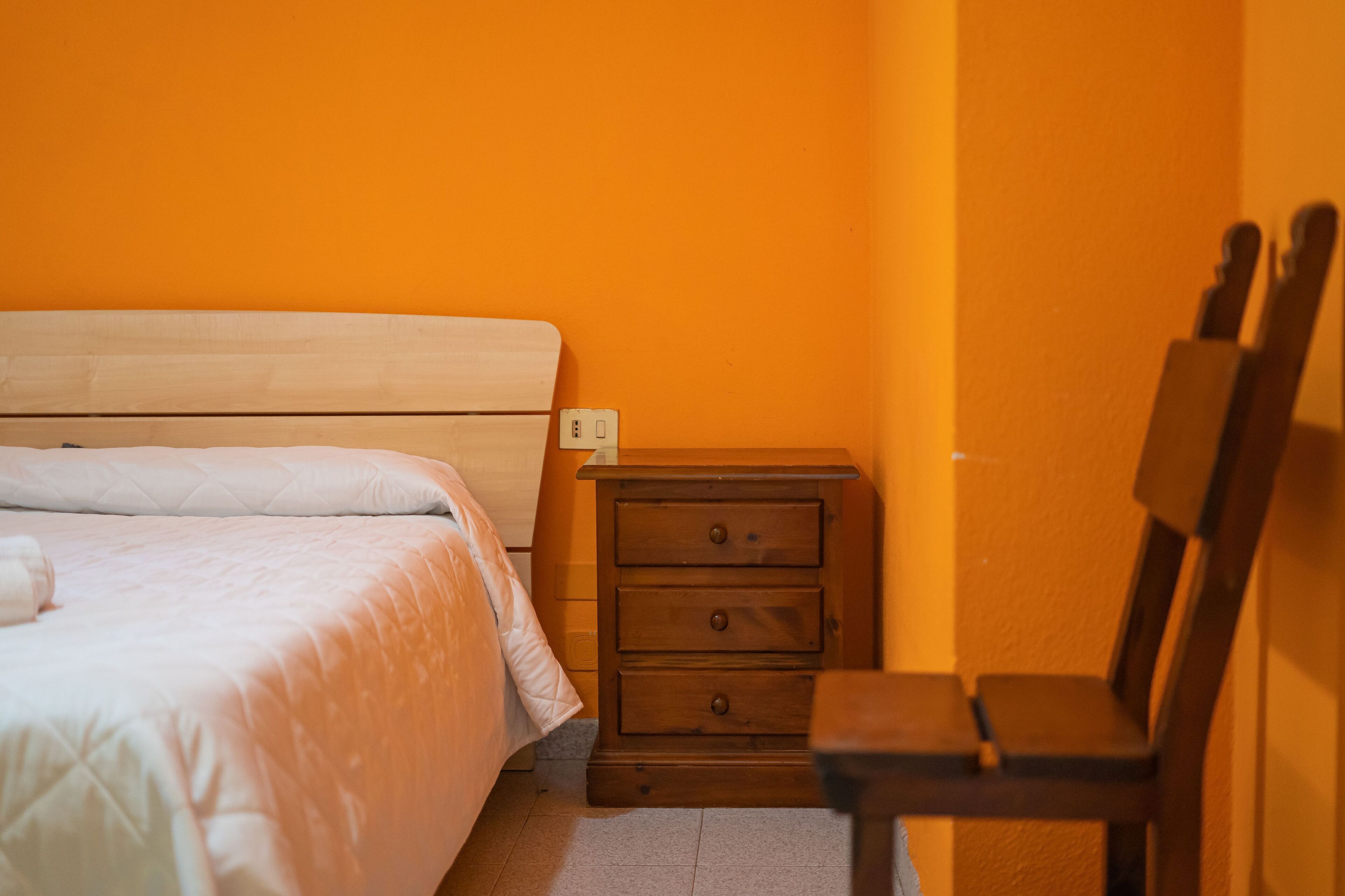A bedroom with a wooden bed, a nightstand with drawers, and a chair.