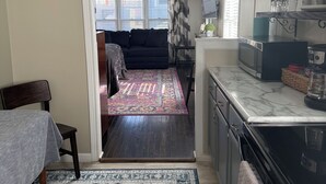 A compact kitchen with a microwave, stove, and countertop. A patterned rug leads to a living area with a couch and a TV. - Charming cottage in central Lafayette 8 min to Purdue (Lafayette)