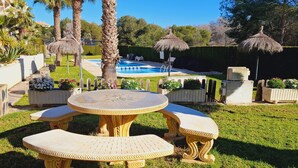 Zona de piscina con pared de piedra, palmeras y una mesa redonda con bancos.