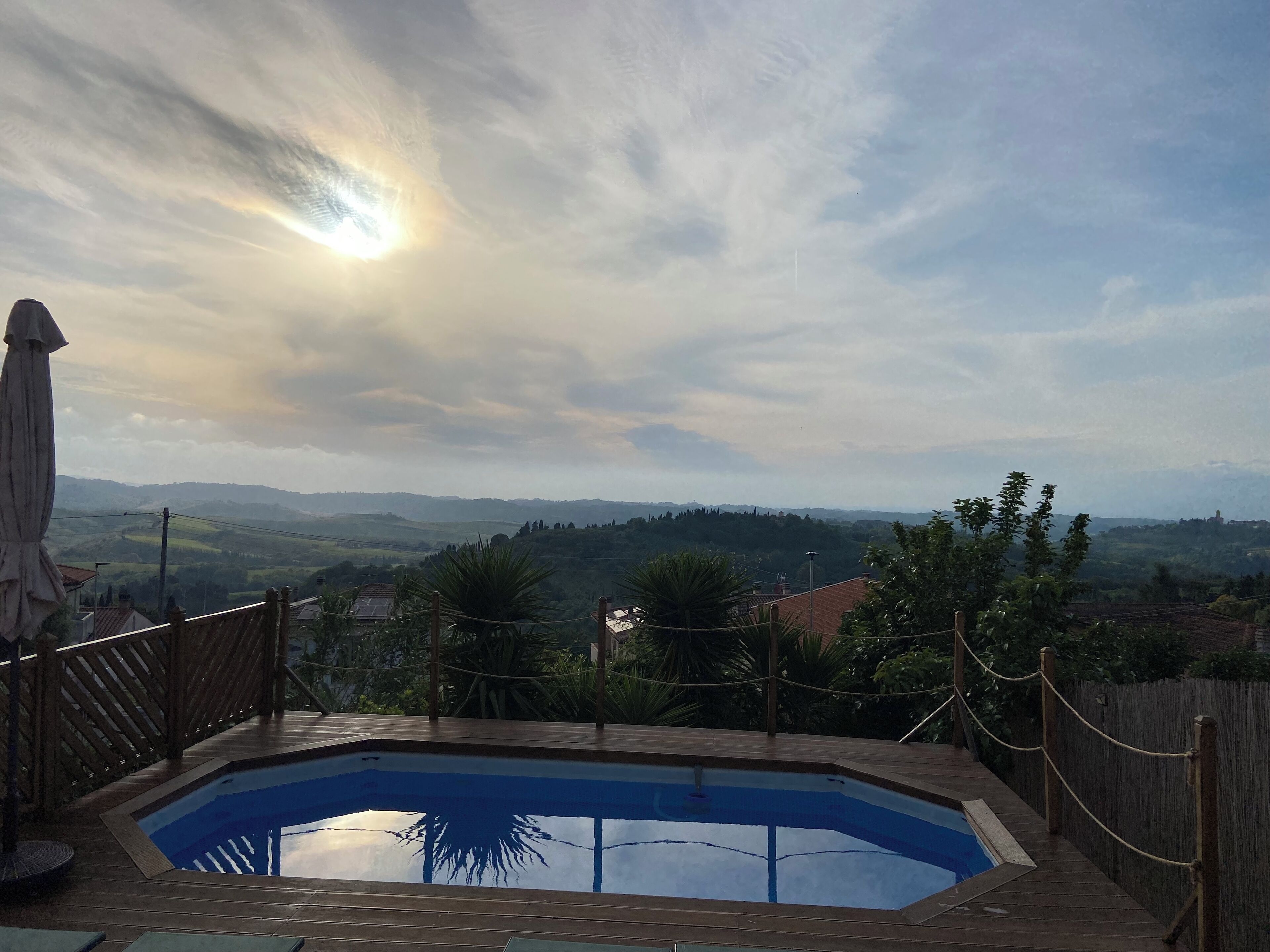 A swimming pool with a wooden deck and a view of distant hills.