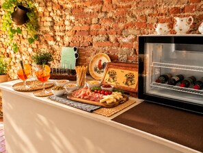 Una zona de bar con pared de ladrillo, un refrigerador lleno de botellas y diversos productos alimenticios y bebidas sobre la barra.