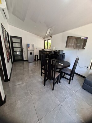 A compact kitchen with a refrigerator, microwave, and stove, a dining area with a table and chairs, and a wall-mounted TV. - NEW! Moody’s – Your Little Piece of Paradise (Savegre)