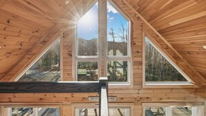 Habitación de madera en el ático con un tragaluz y ventanas amplias que ofrecen vistas a un paisaje montañoso.